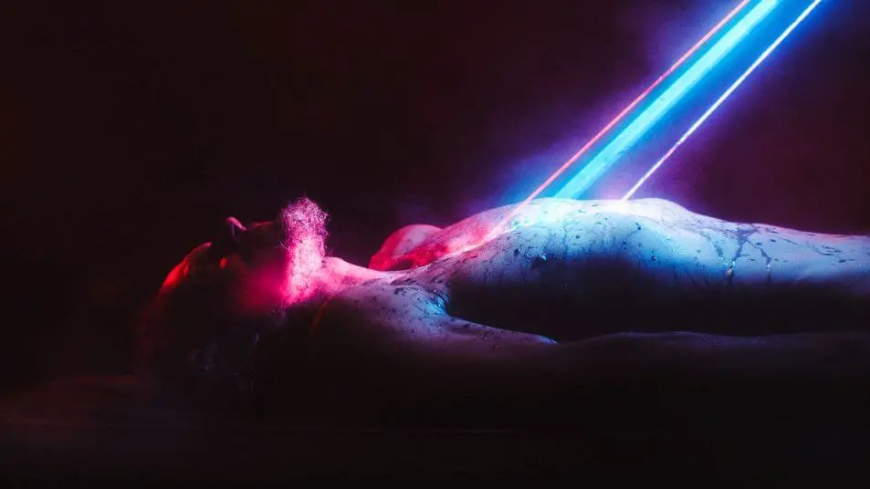 Image of lasers scanning the body of a shirtless man on a table in the Shudder original Fried Barry.