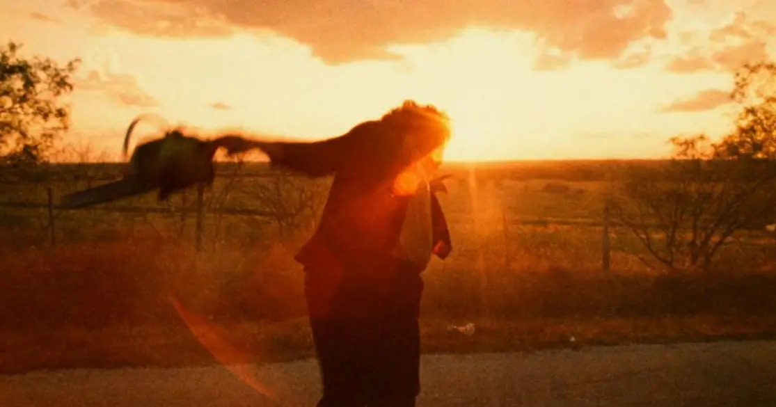 At sunset, a hulking man in a suit wildly swings a running chainsaw in this scene from Tobe Hooper's The Texas Chain Saw Massacre (1974).