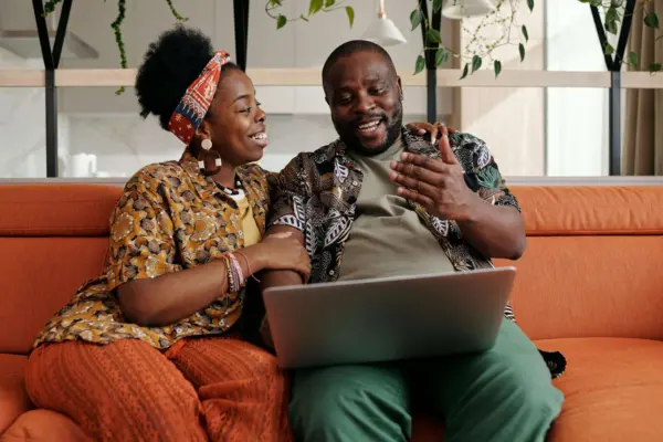 Couple on couch looking at laptop and smiling