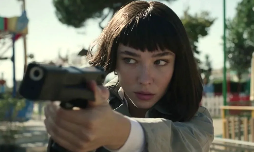 A woman with straight-across bangs holds a gun.